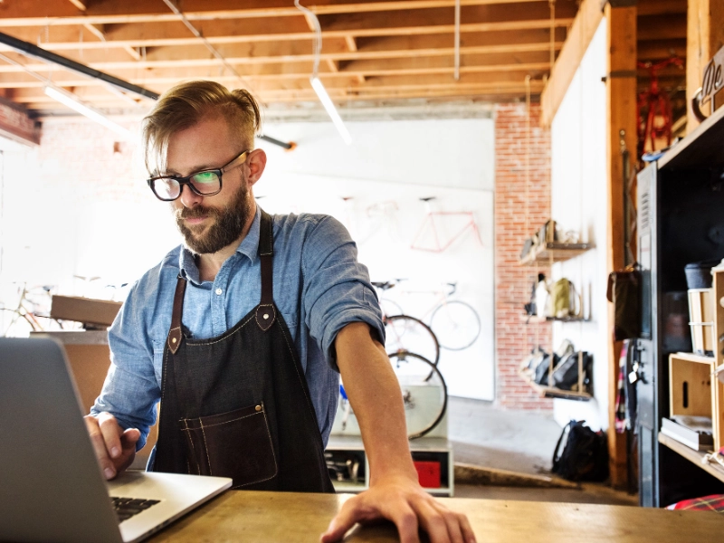 Fachhändler im Fahrradgeschäft steht am Tresen und schaut komnzentriert in den Laptop. Er nutzt die Partner API