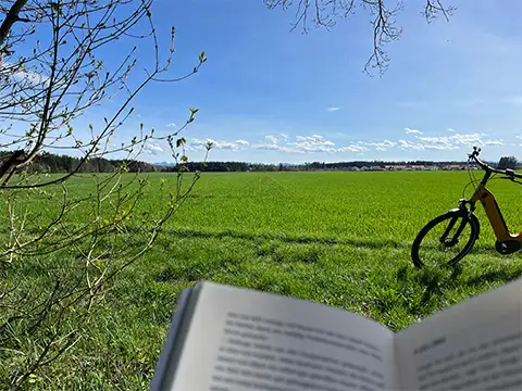 Mit dem JobRad und einem Buch bei einer Wiese im Sonnenschein