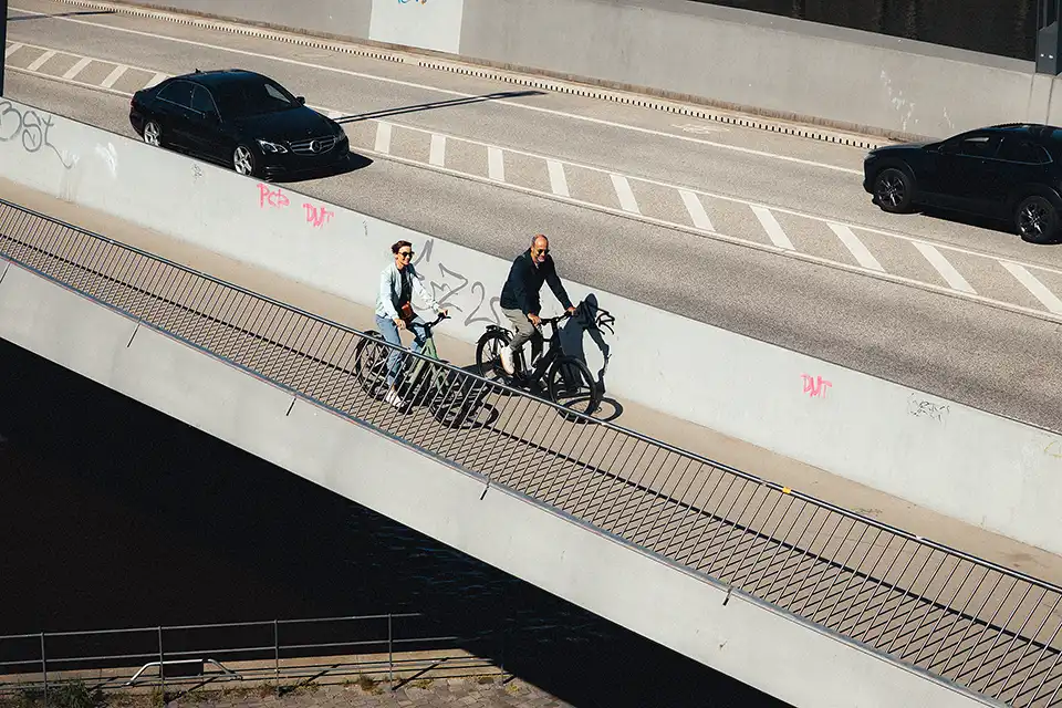 Zwei Radfahrer:innen auf einer Brücke neben einer großen Straße